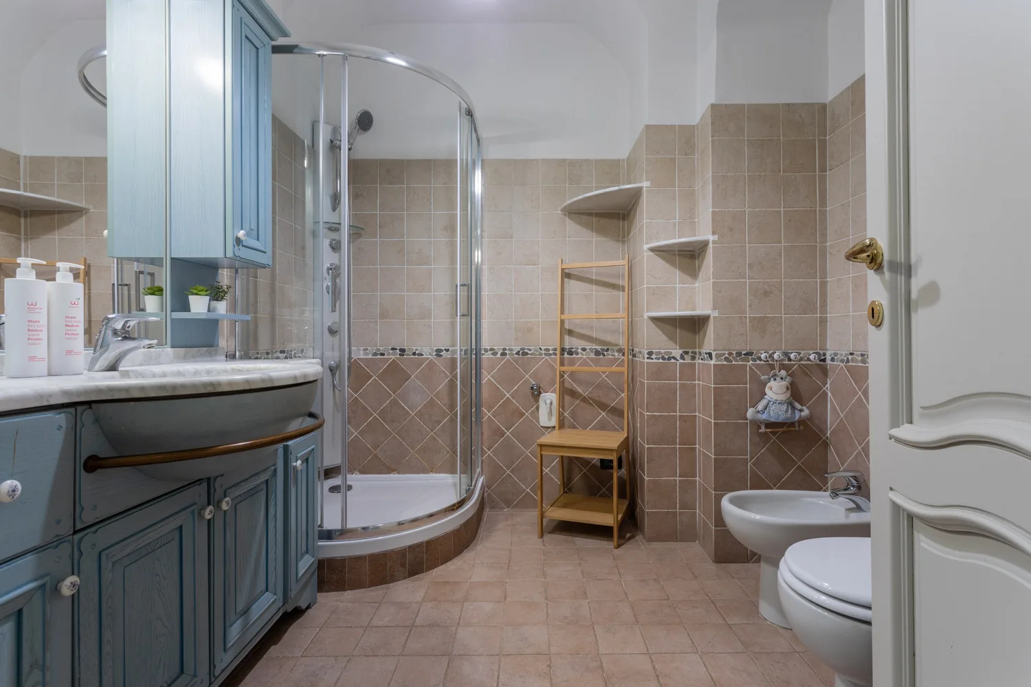 A tiled bathroom with a sink, curved shower enclosure, and toilet.
