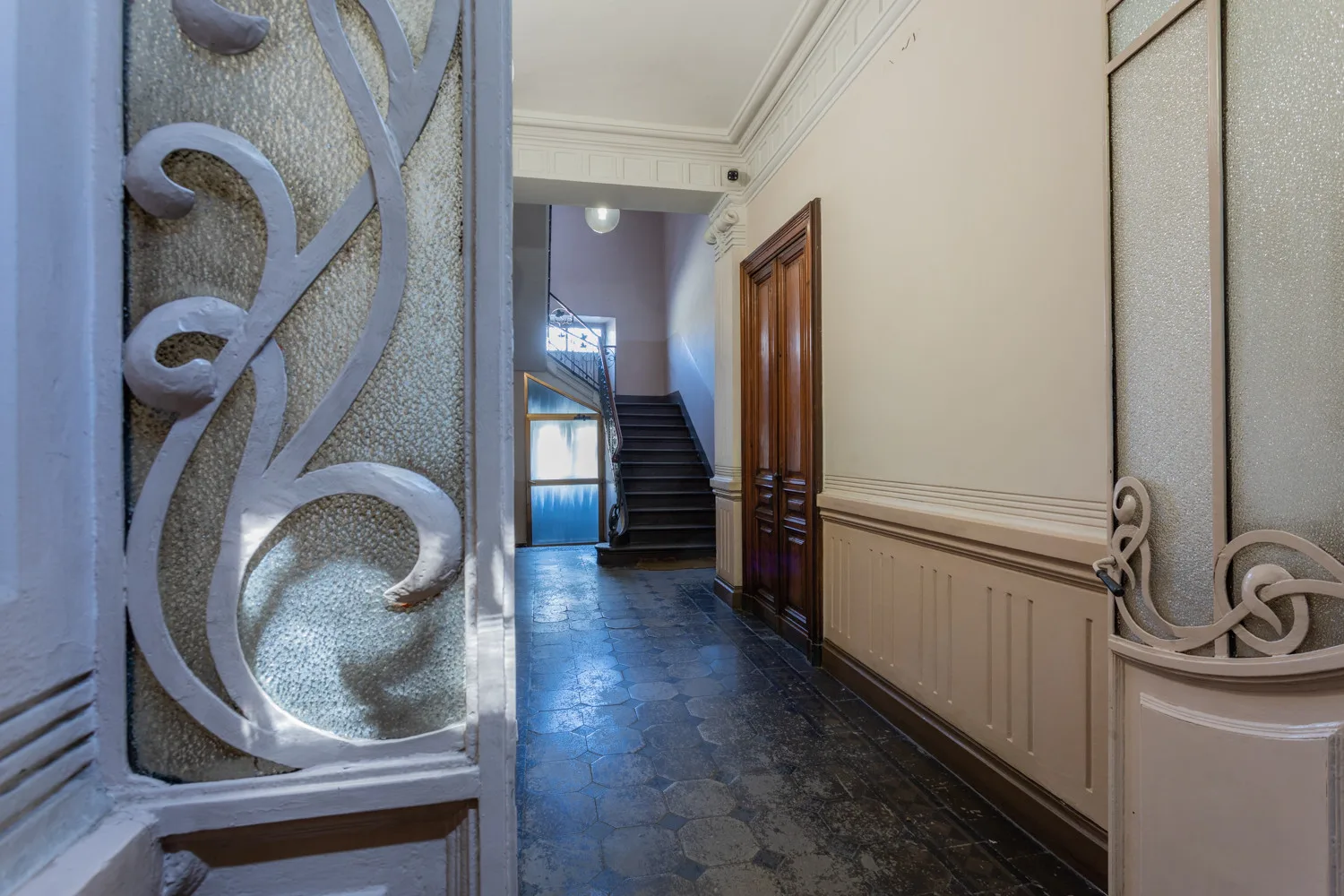 An interior hallway with decorative panels, wooden doors, and stairs at the far end.