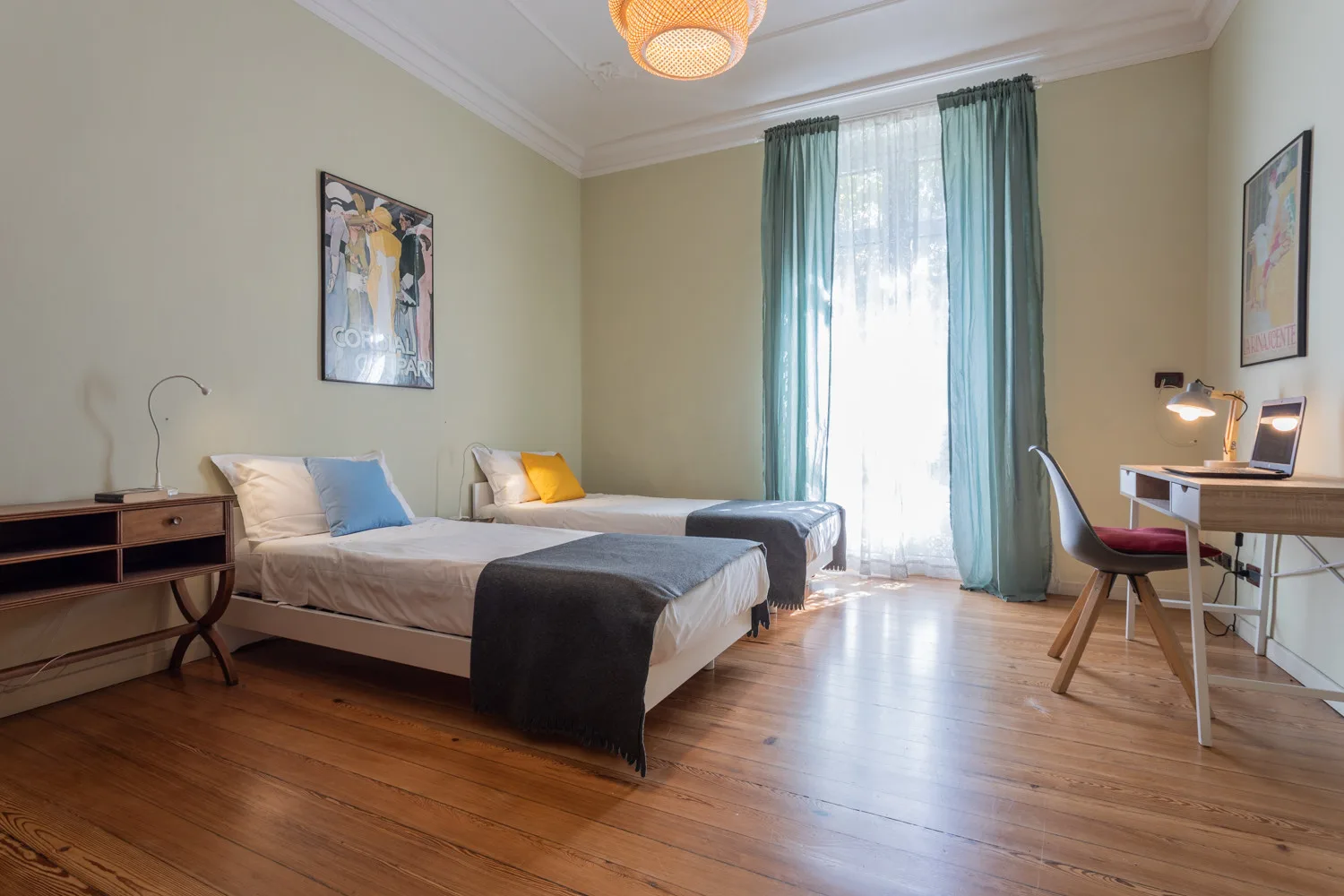 A bedroom with two beds, a desk, and curtains framing a tall window.