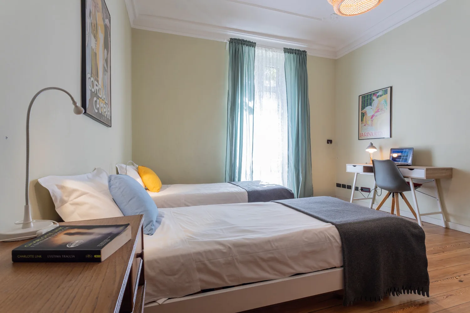 A bedroom with beds, a desk, and a window with blue curtains.