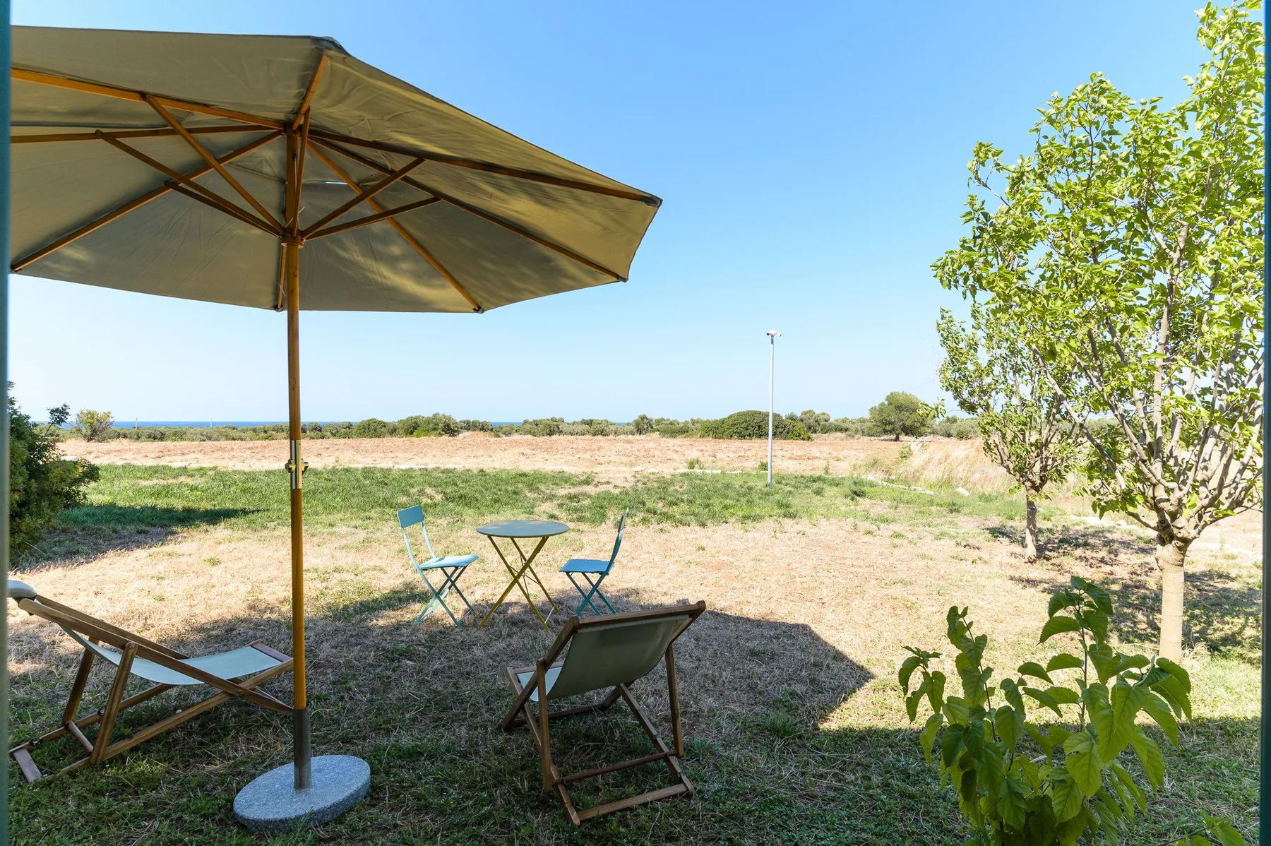 An outdoor seating area sits beneath a large umbrella, overlooking a grassy field.