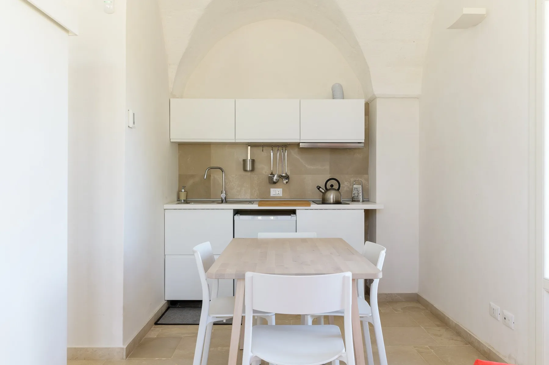 A bright dining area with a table and a compact kitchen at the back.