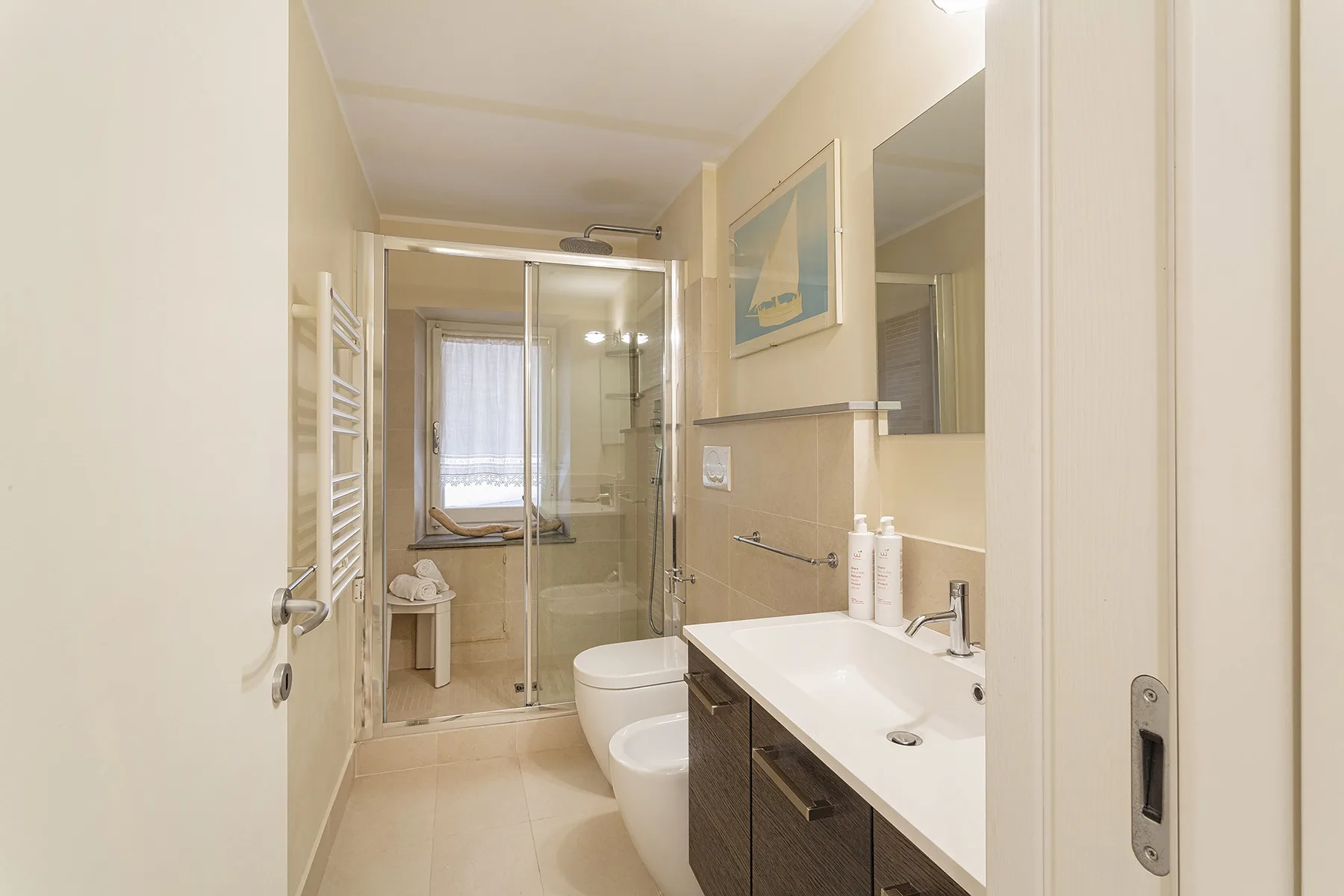 Un baño luminoso con ducha de vidrio, inodoro y un lavabo alargado.