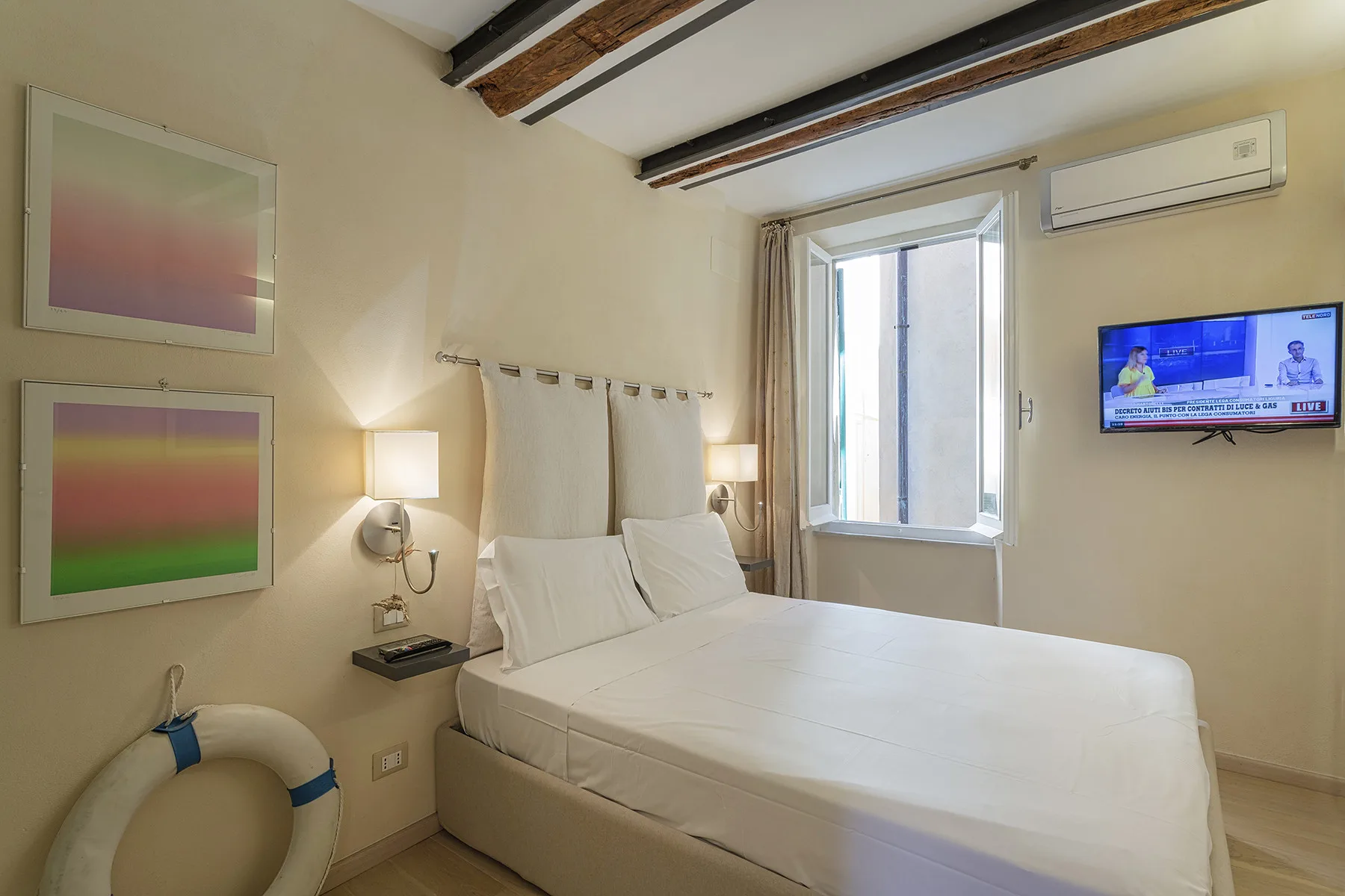 Un dormitorio con una cama grande, una ventana con cortinas y un televisor en la pared.
