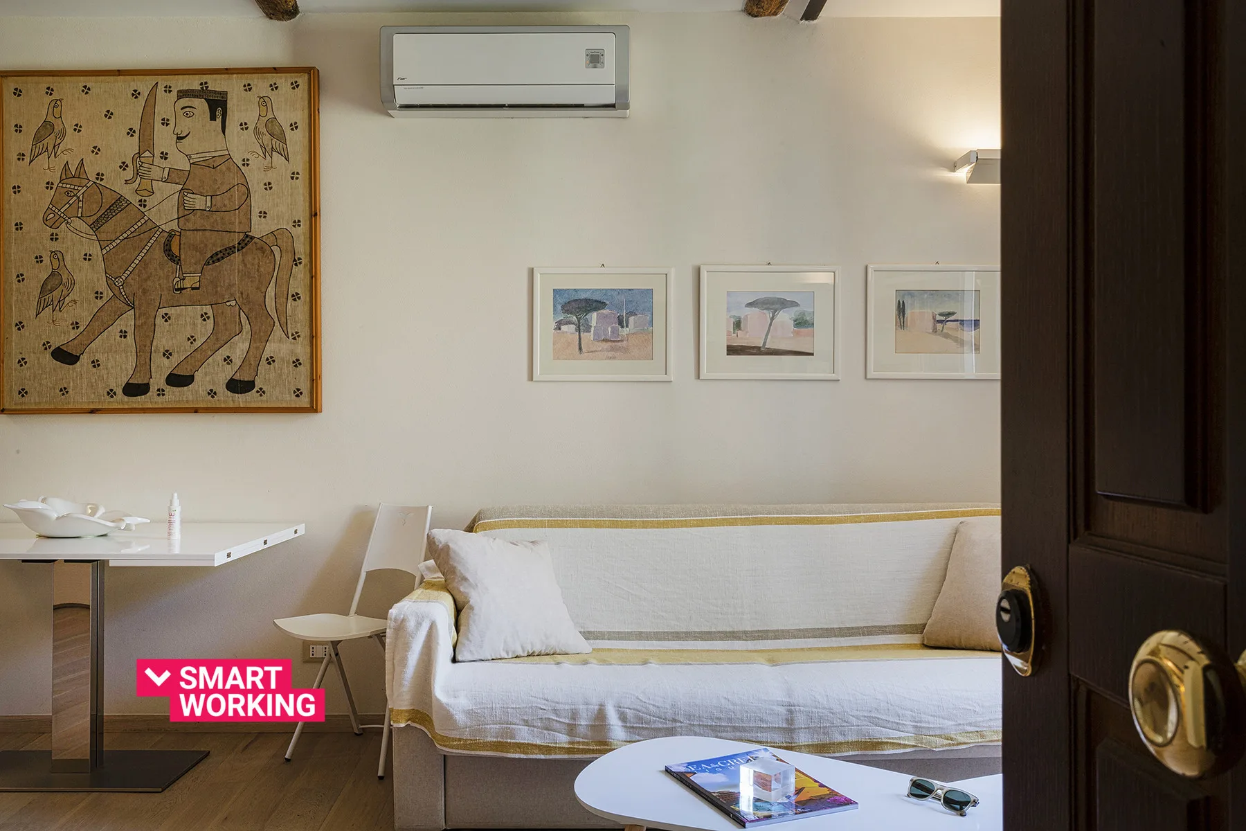 Una sala de estar con diván, cuadros enmarcados y aire acondicionado en la pared.