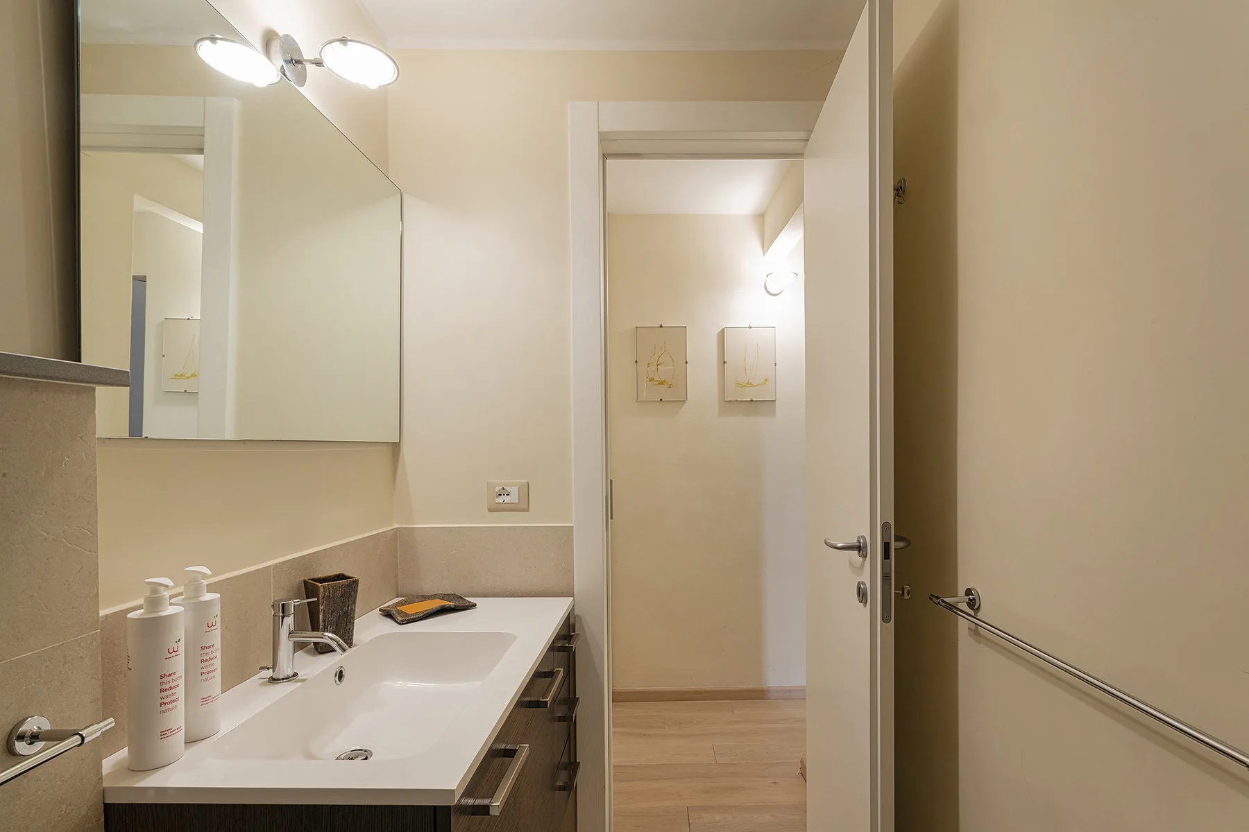 Un tocador de baño con lavabo y espejo junto a una puerta abierta.