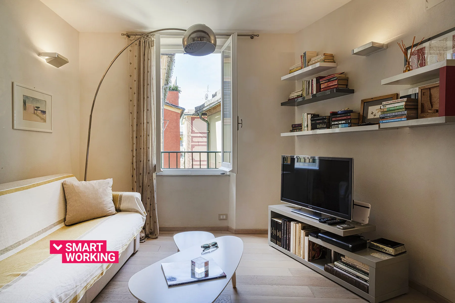 Una sala luminosa con sofá, mesa de centro y televisor junto a una ventana abierta.