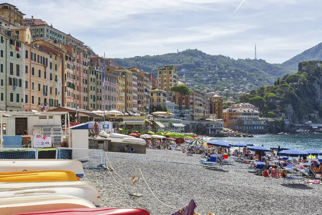 Una playa junto al mar, con edificios coloridos junto a la costa y colinas al fondo.
