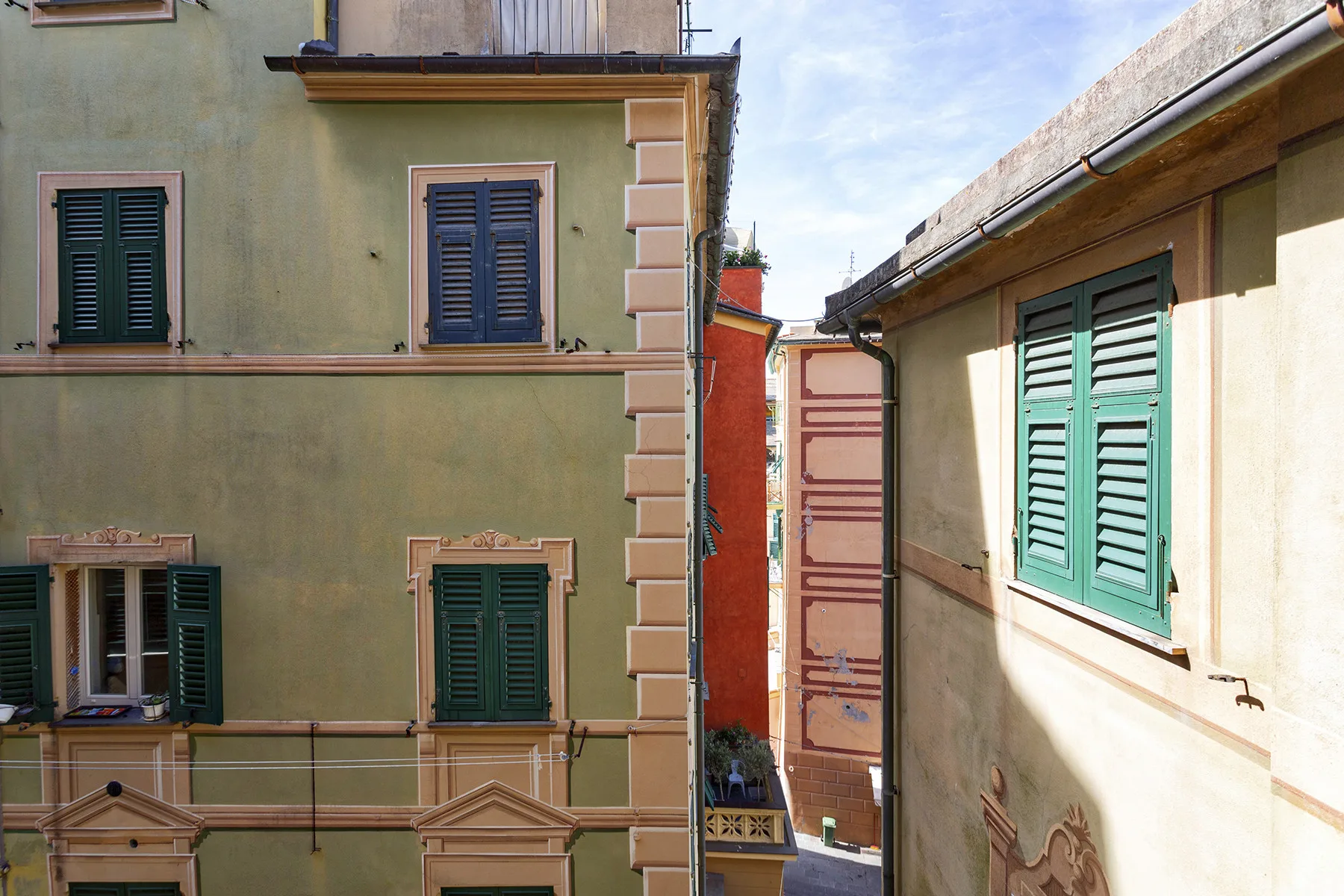 Un pasaje estrecho entre fachadas pintadas con ventanas con contraventanas.