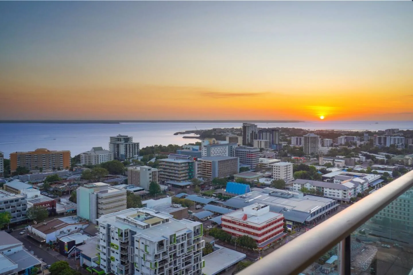 A sunset over the coastline and city buildings, viewed from a balcony.