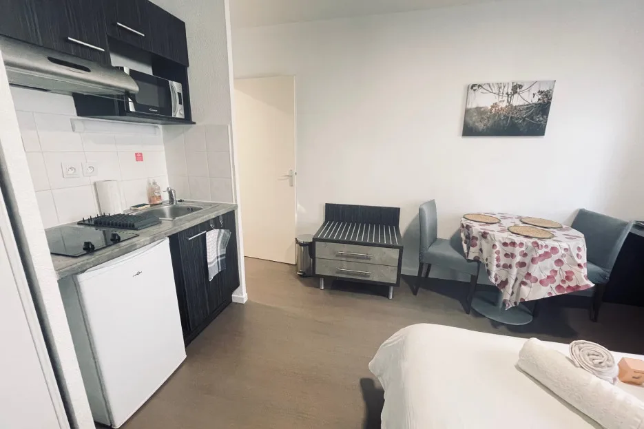 A compact room has a kitchenette, dining table, seating, and a bed.