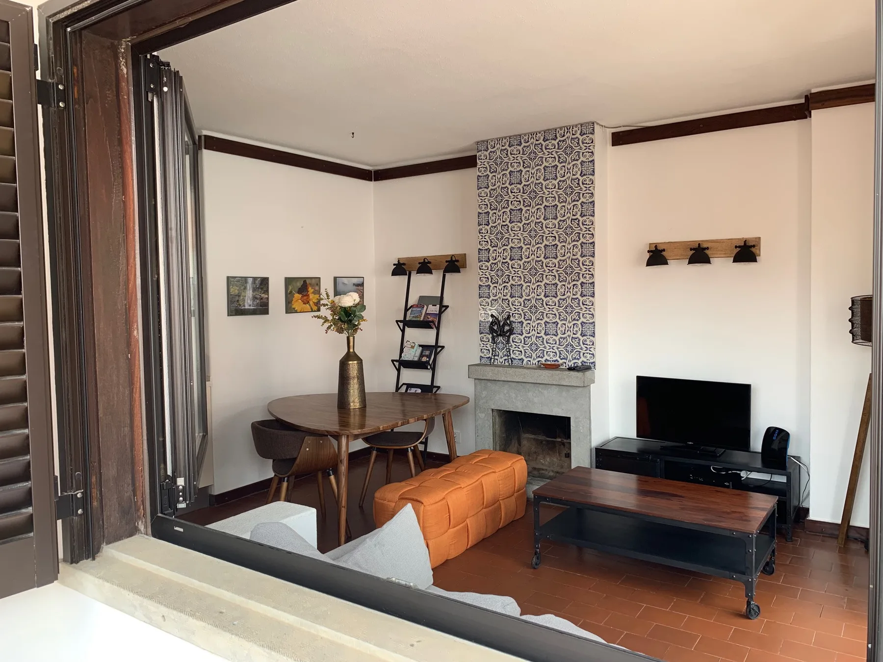 Una sala de estar con mesa de comedor y televisión junto a una chimenea decorada con azulejos.