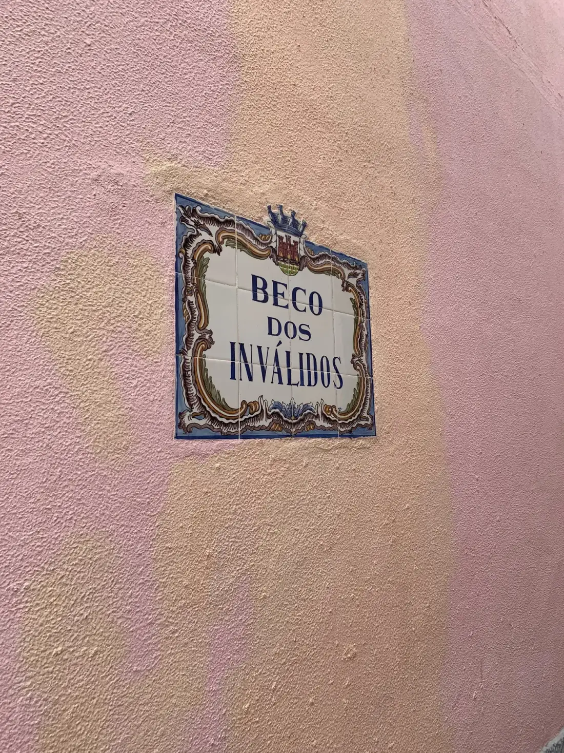 Una placa con el texto «Beco dos Inválidos» está montada en una pared rosa.