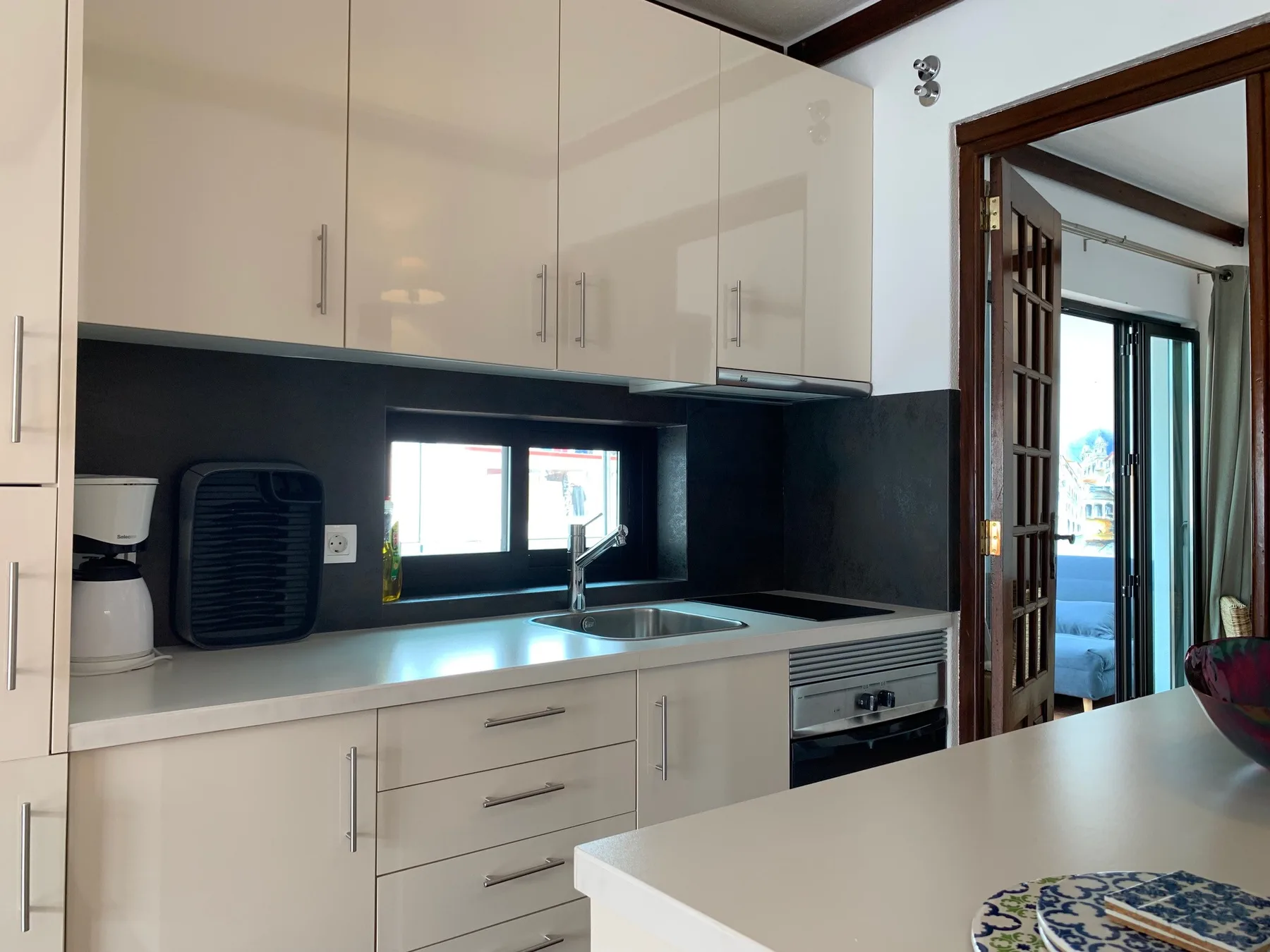 Cocina luminosa con armarios blancos, una encimera y un fregadero bajo una ventana.