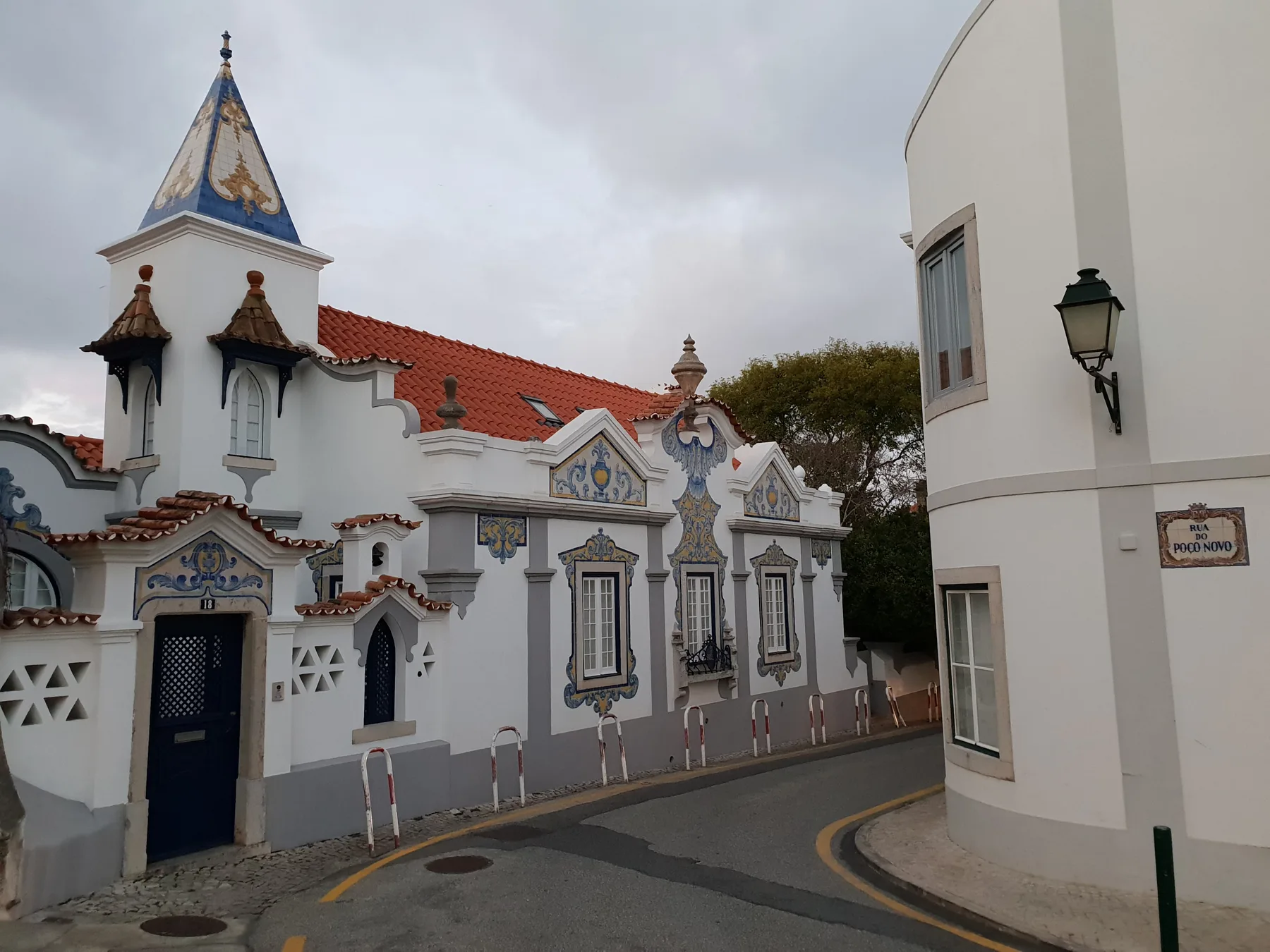 Una calle curva junto a un edificio blanco con adornos azules y una torre puntiaguda.