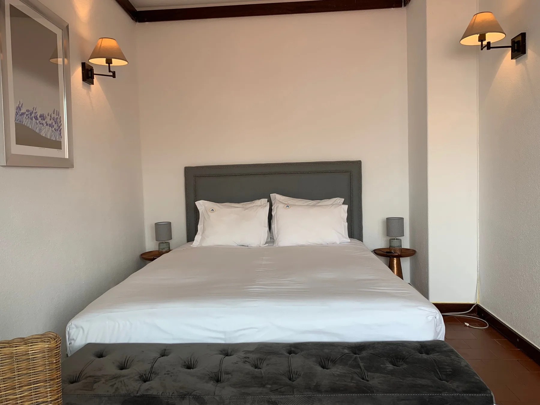 Un dormitorio con una cama bien tendida y un banco tapizado oscuro.