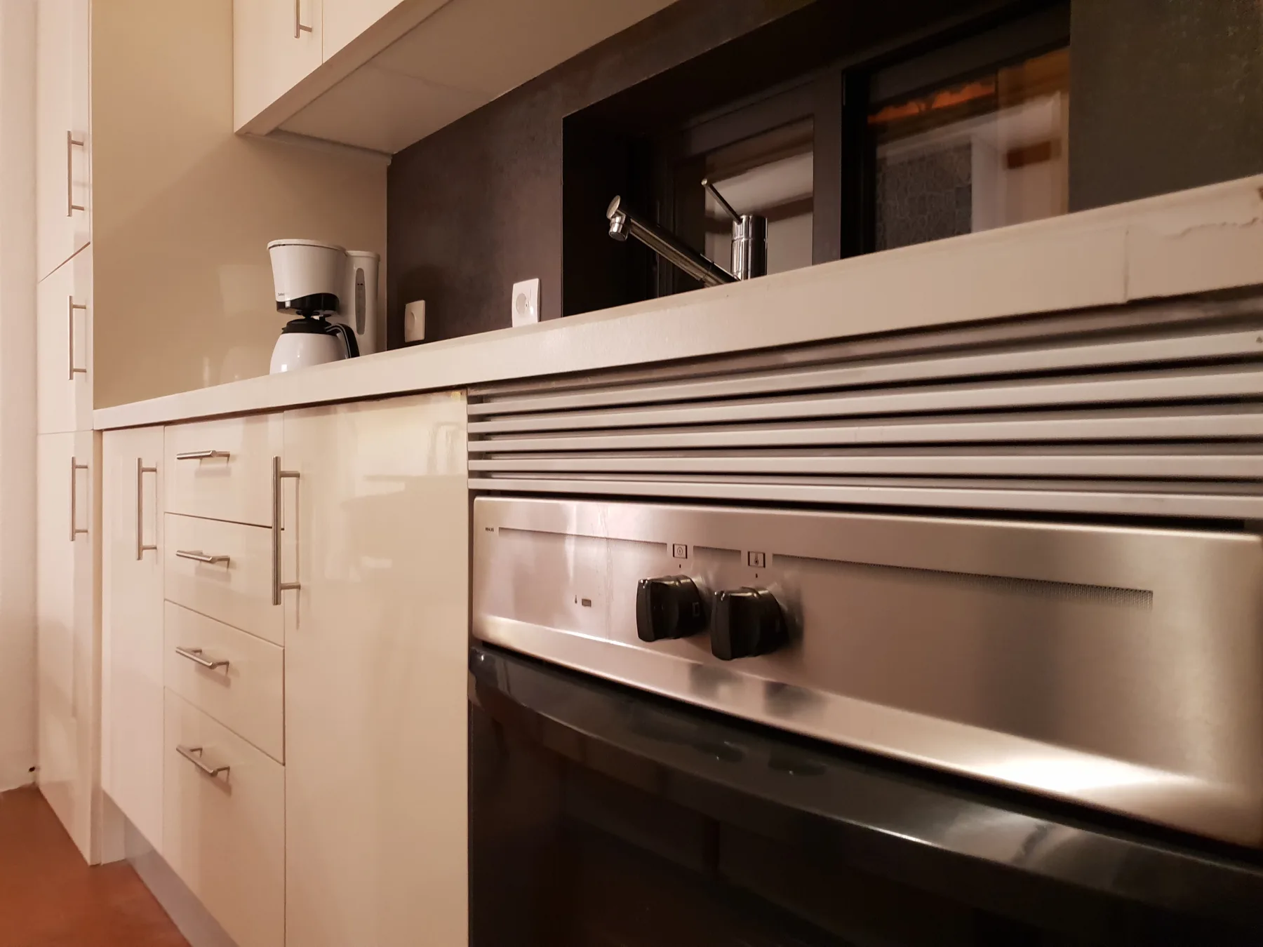 Una cocina moderna con gabinetes brillantes, un horno empotrado y una cafetera.