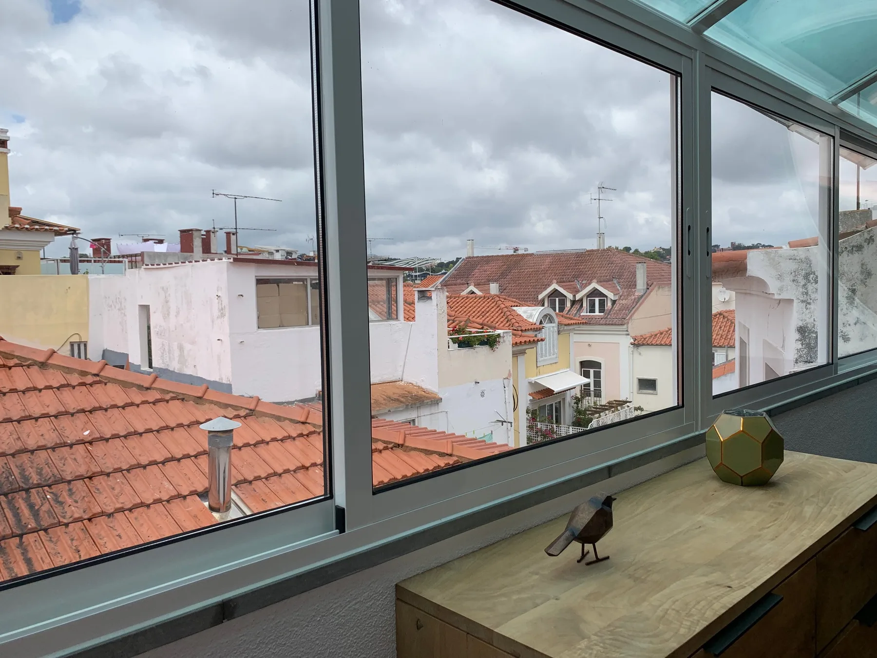 Una ventana amplia da a tejados de tejas y edificios cercanos bajo un cielo nublado.