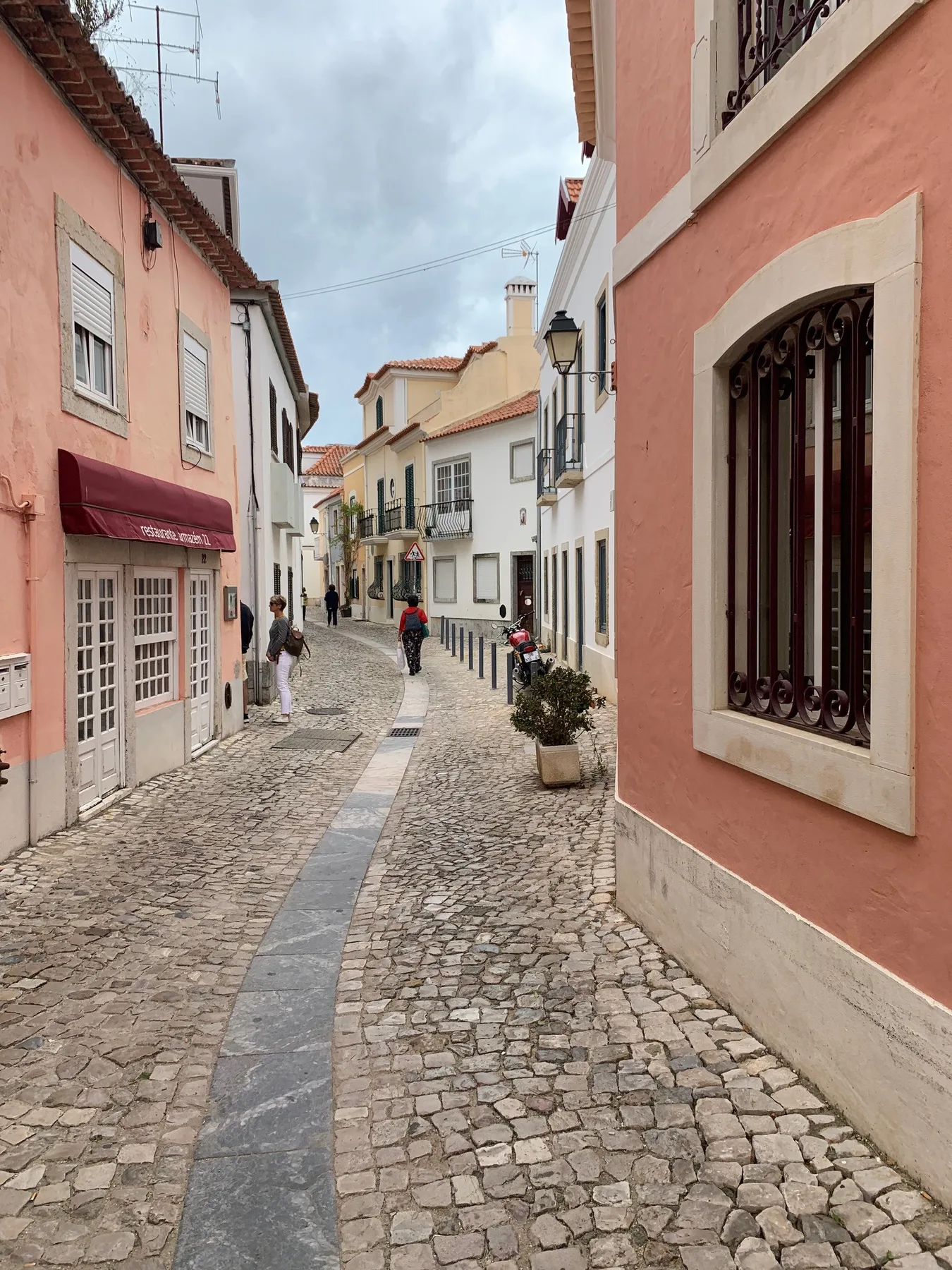 Una calle empedrada pasa entre edificios de tonos pastel en una vía estrecha.