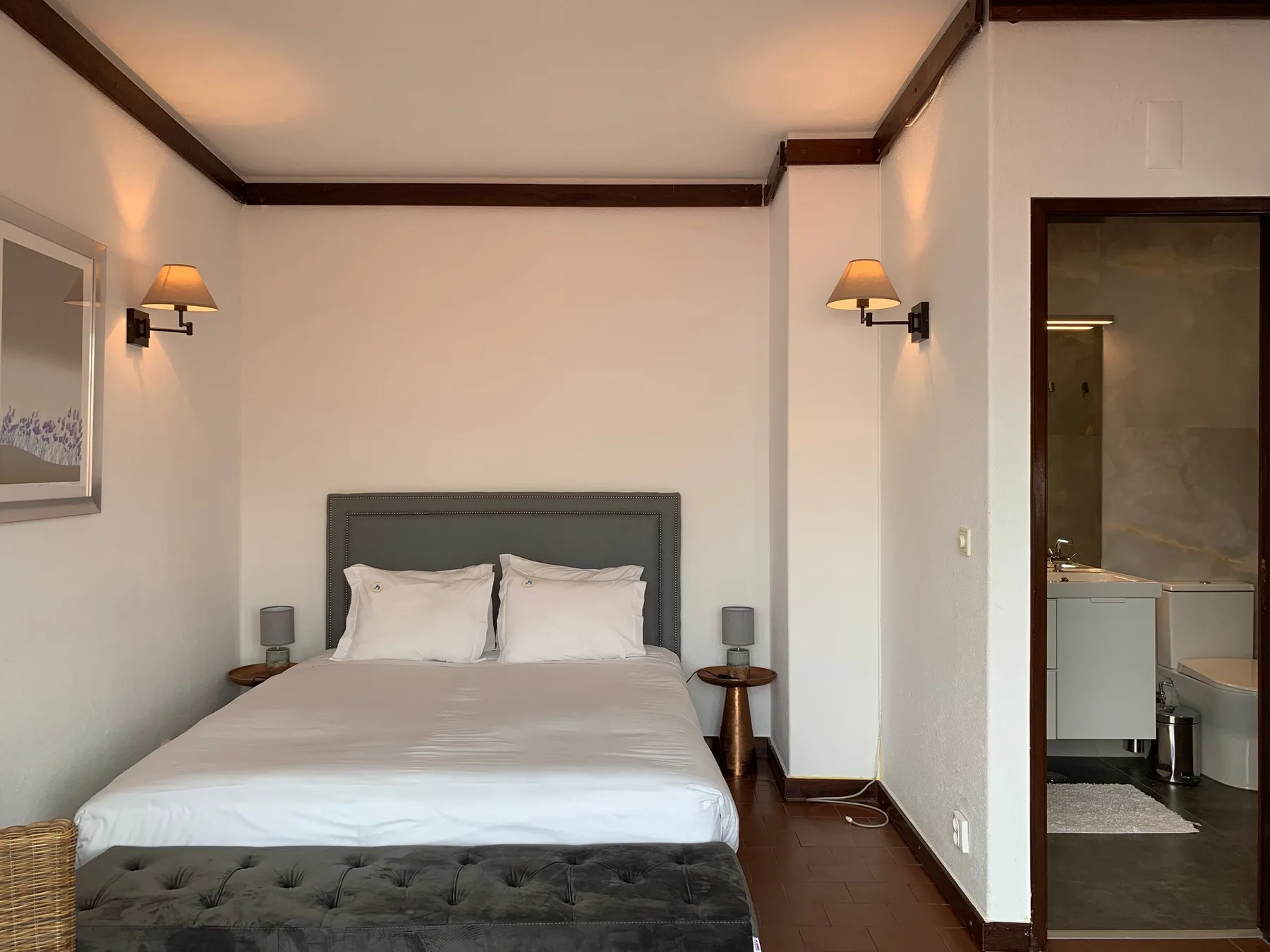 Dormitorio con una cama bien arreglada y un banco oscuro tapizado a los pies.