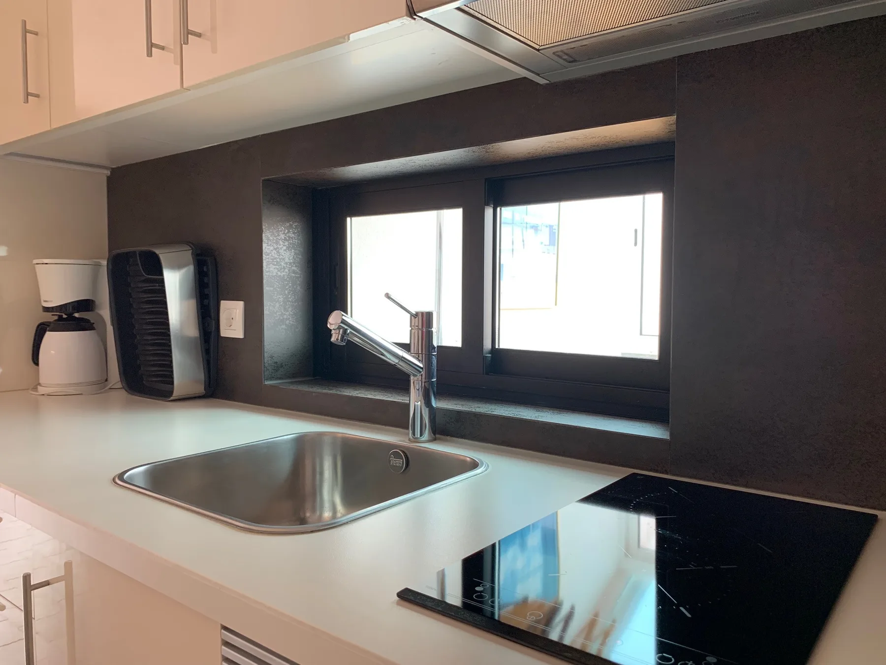Una encimera de cocina con fregadero, grifo y placa de cocción bajo una ventana.