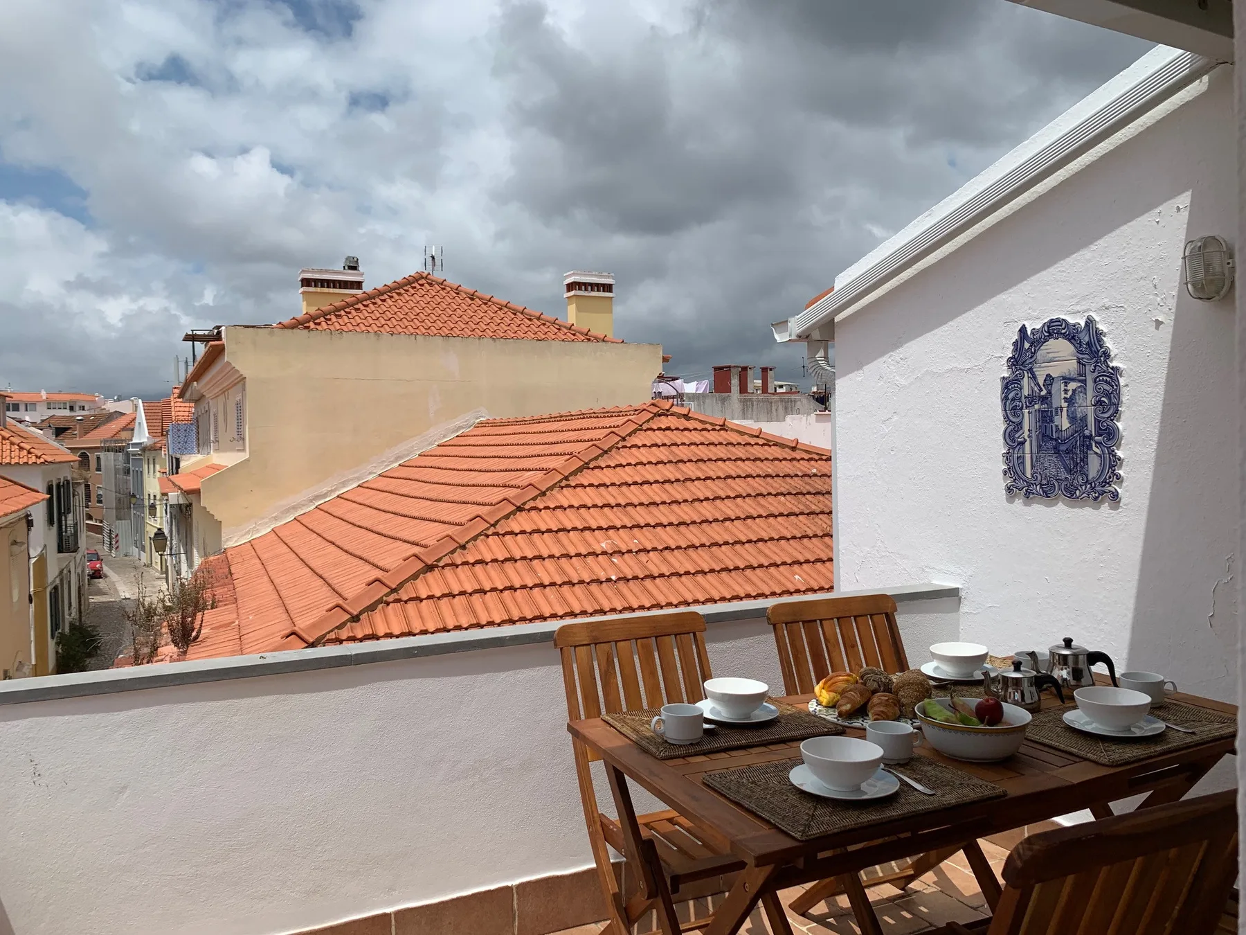 Una terraza en la azotea da a tejados de terracota, con una mesa puesta con platos.
