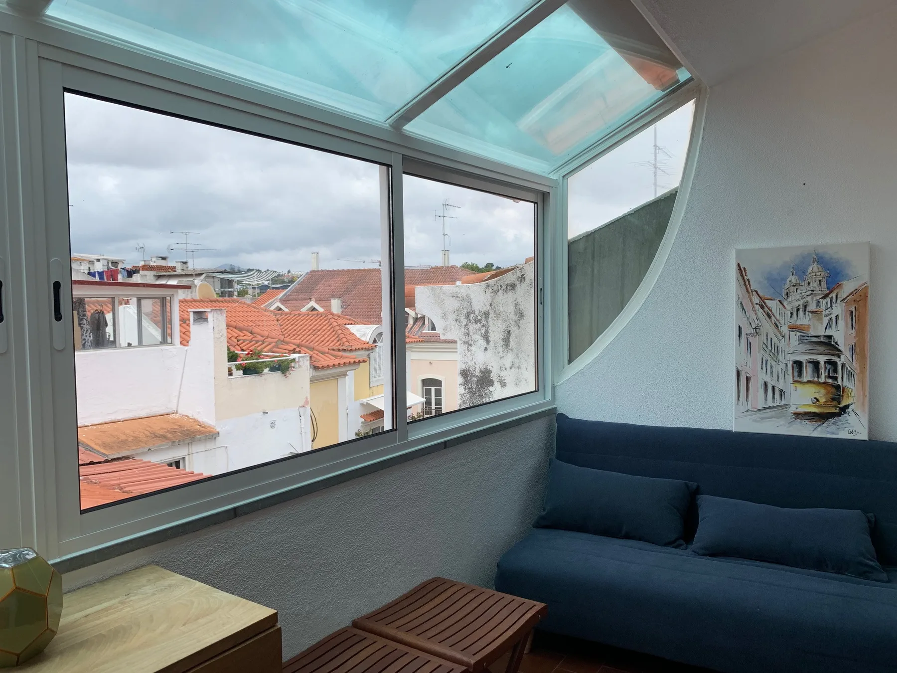 Una zona de estar con grandes ventanas tiene un sofá azul oscuro y vistas a los tejados cercanos.