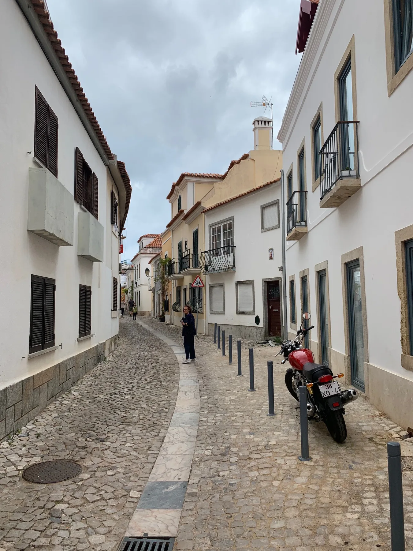 Una estrecha calle empedrada flanqueada por edificios blancos y motos aparcadas.