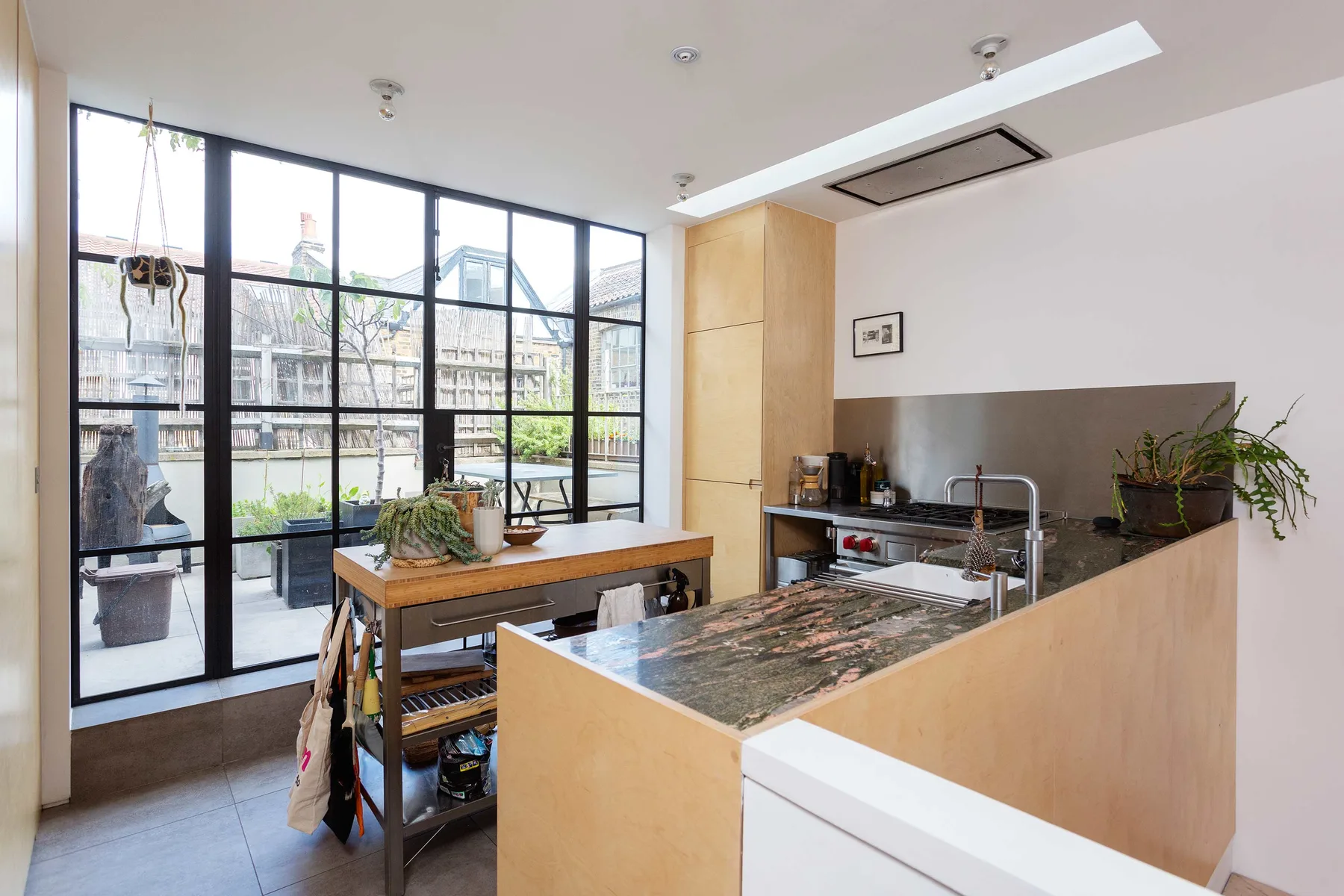 Una cocina luminosa con una isla larga y grandes ventanales que dan a un patio.