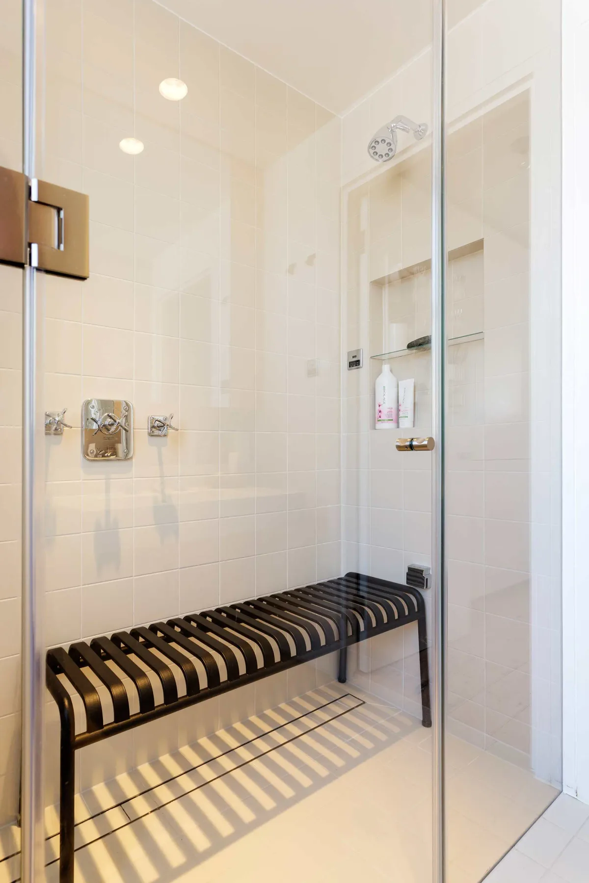 Zona de ducha con azulejos, un banco integrado y accesorios en la pared.