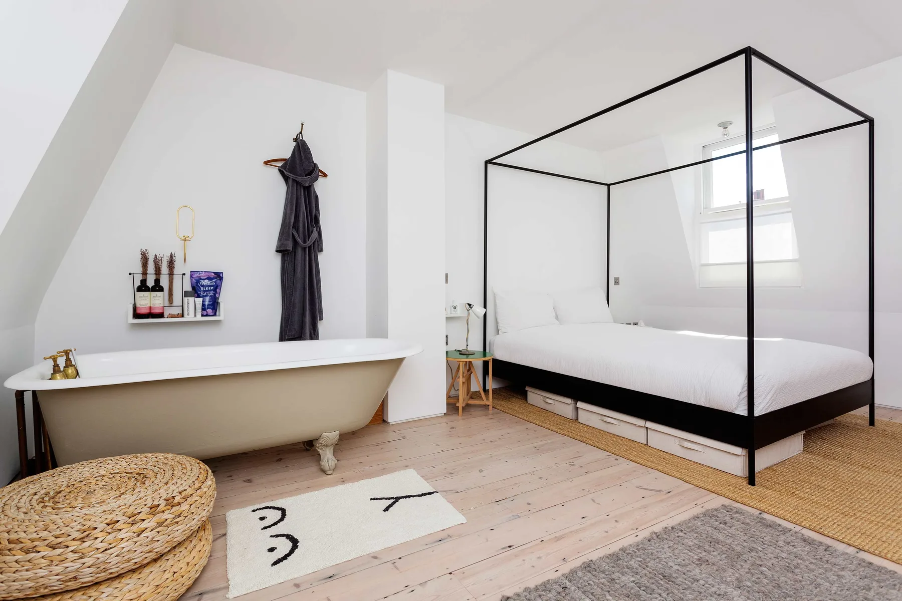Un dormitorio luminoso con cama con dosel, bañera exenta y alfombras tejidas.