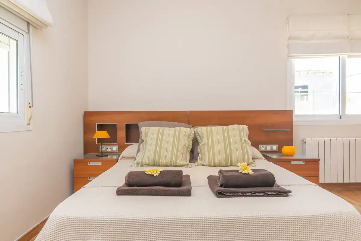 Un dormitorio con una cama, mesitas de noche y ventanas.