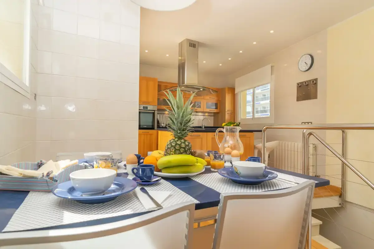 Una mesa de comedor está puesta frente a una cocina luminosa.