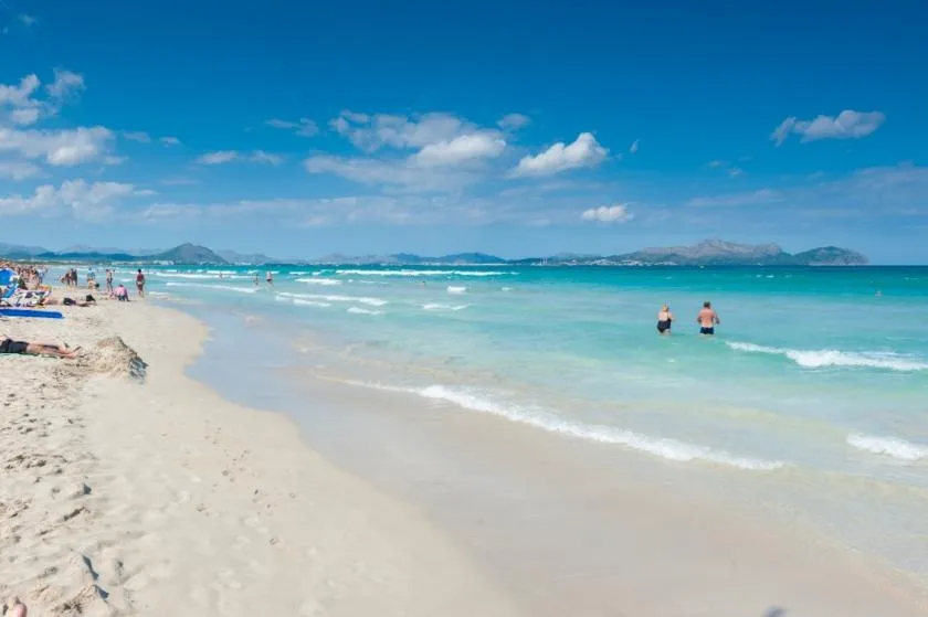 Una playa de arena se encuentra con aguas turquesas poco profundas bajo un cielo parcialmente nublado.
