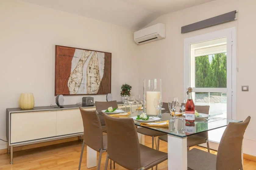 Comedor con una mesa de vidrio y varias sillas junto a una ventana amplia.