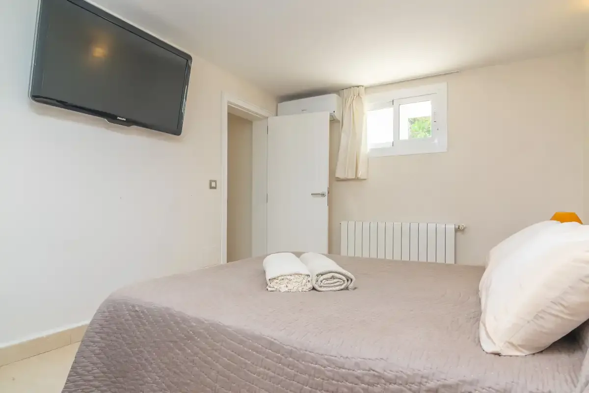 Un dormitorio con una cama, un televisor en la pared y una ventana sobre un radiador.