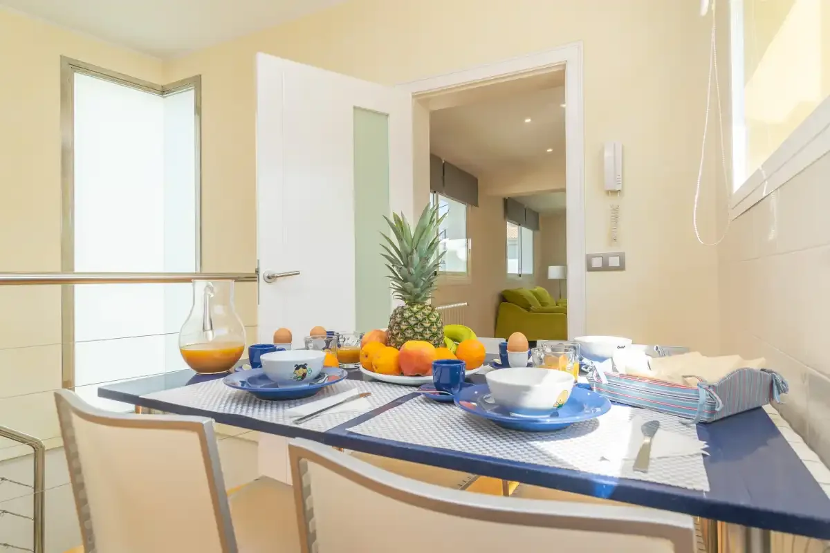 Una mesa de comedor está puesta con platos, fruta y una piña junto a una puerta abierta.