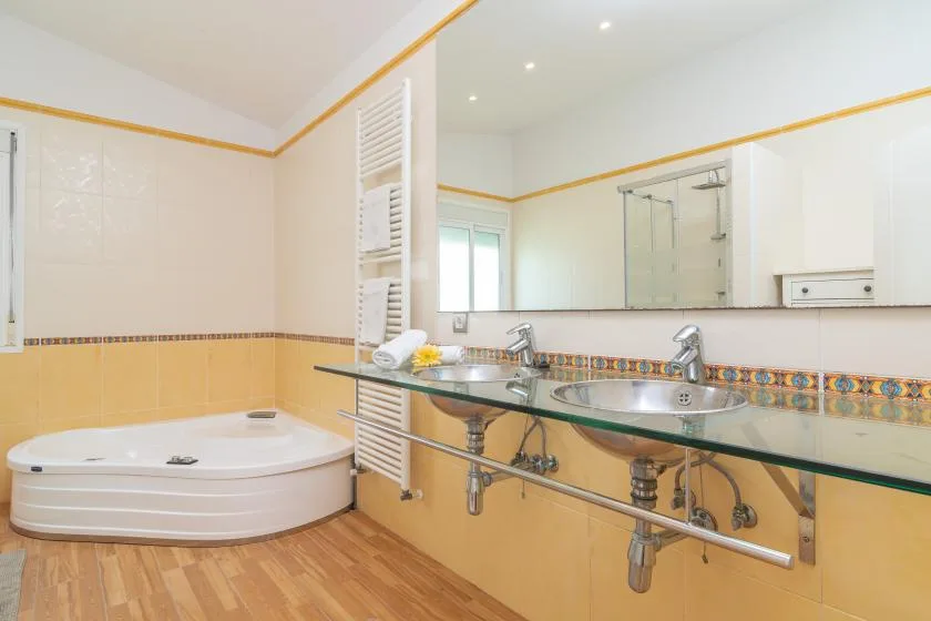 Un baño con azulejos tiene una bañera de esquina, una ducha de vidrio y un lavabo largo.