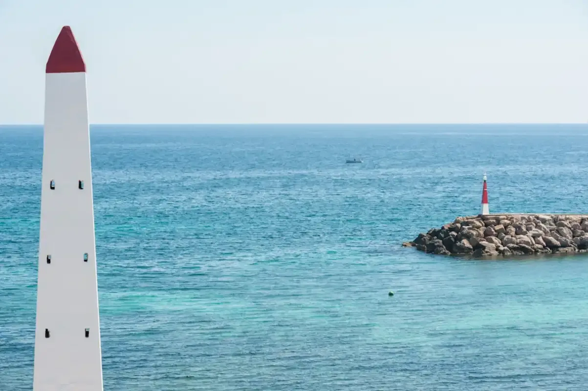 Un faro blanco y rojo se alza junto al mar azul.