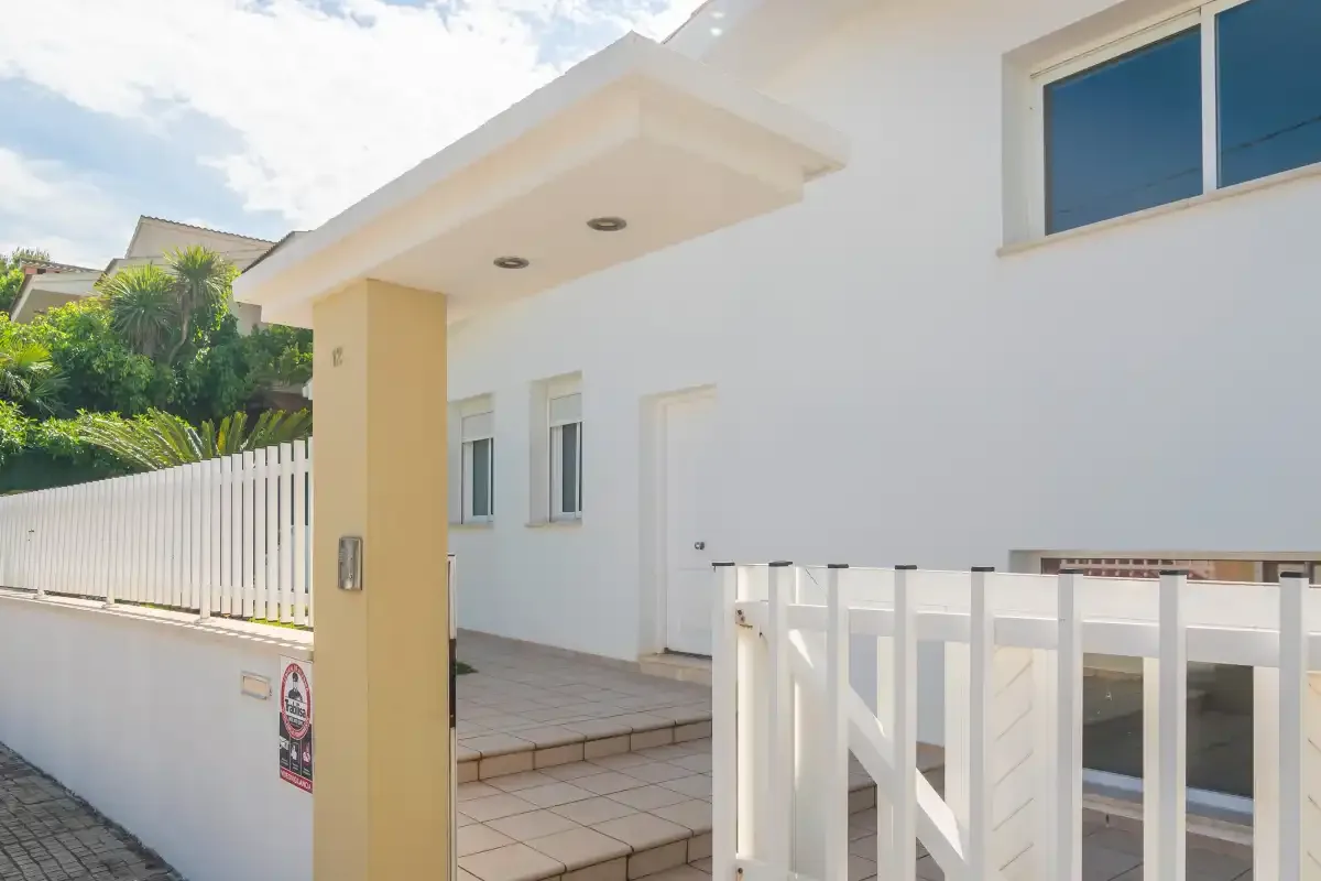 La entrada de una casa blanca con porche de baldosas y una puerta blanca.