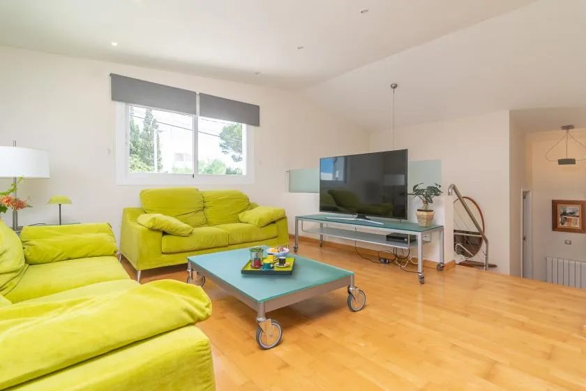 Una sala luminosa con asientos verdes, una mesa de centro y un televisor.