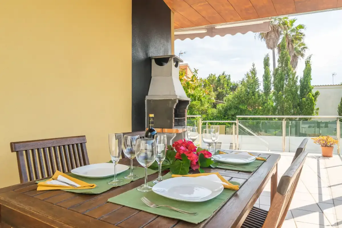 Comedor exterior cubierto con la mesa puesta y vistas al jardín.