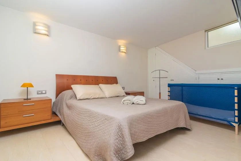 Un dormitorio luminoso con una cama grande, una mesita y una barandilla azul.