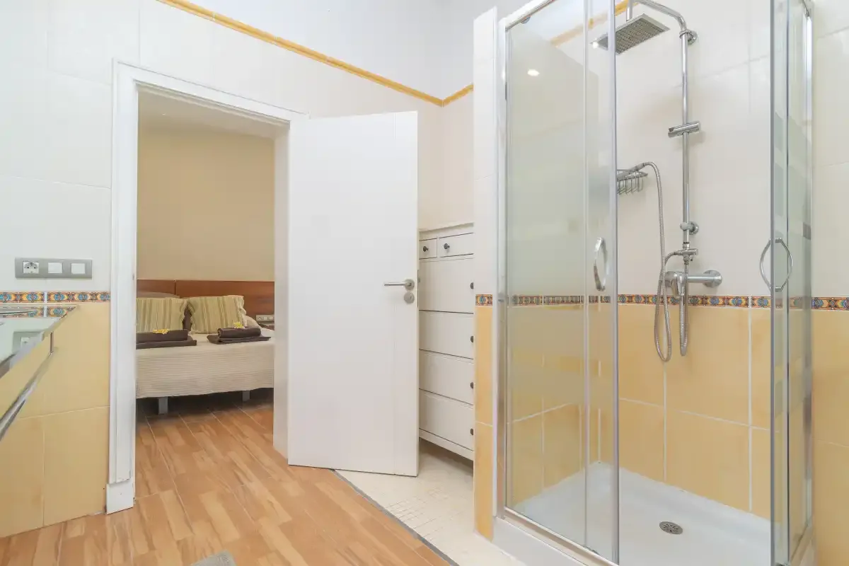 Un baño con una ducha de cristal y una puerta abierta a un dormitorio.