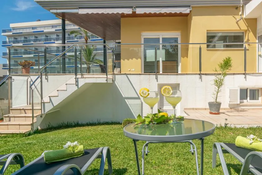 Un patio ajardinado con asientos al aire libre, una mesa de cristal y un edificio amarillo detrás.