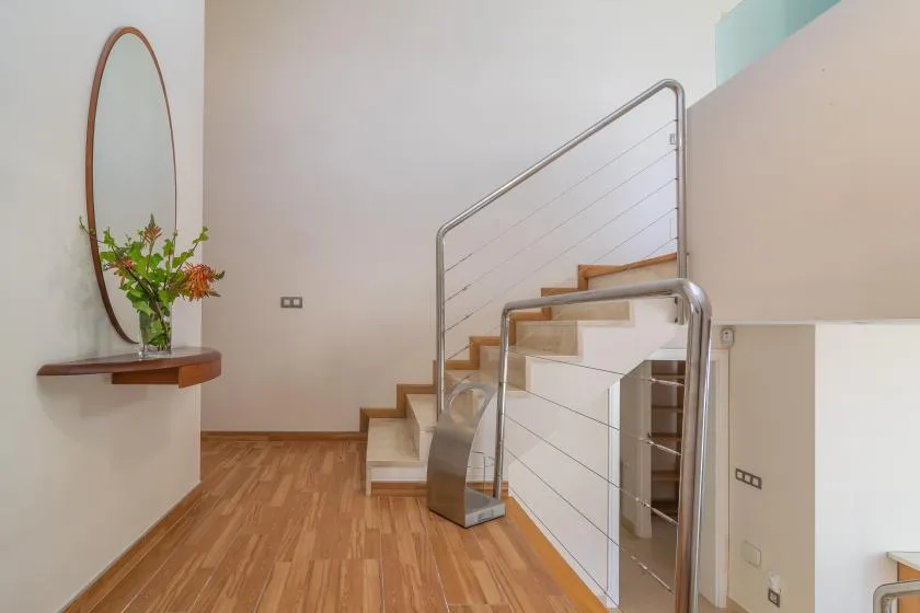 Una escalera interior luminosa con barandillas metálicas y suelo de madera.