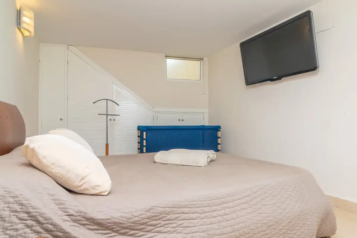 Un dormitorio con una cama y un televisor montado en la pared.