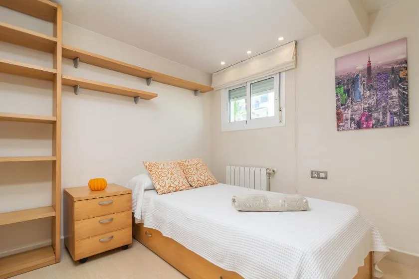 Un dormitorio luminoso con una cama, estanterías empotradas y una ventana pequeña.