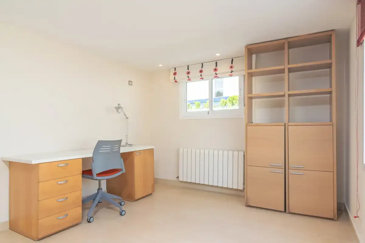 Un estudio luminoso con escritorio, silla de oficina y estantería alta.