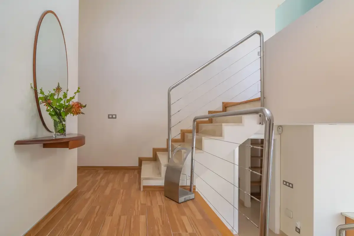 Pasillo interior con suelo de madera y una escalera con barandillas metálicas.